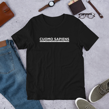 Load image into Gallery viewer, A black unisex t-shirt on the floor, featuring the Cuomo Sapiens S.U.D.L.T. SEAL graphic in white.