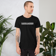 Load image into Gallery viewer, Man standing next to some plants, wearing a black unisex t-shirt, featuring the Cuomo Sapiens S.U.D.L.T. graphic in white.