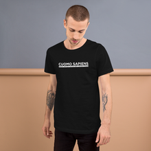 Load image into Gallery viewer, Man standing against a wall, wearing a black unisex t-shirt, featuring the Cuomo Sapiens S.U.D.L.T. graphic in white.