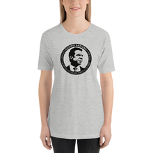Load image into Gallery viewer, Woman wearing a heather grey unisex t-shirt, featuring the Cuomo Sapiens S.U.D.L.T. SEAL graphic in black.