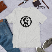 Load image into Gallery viewer, A heather grey unisex t-shirt on the floor, featuring the Cuomo Sapiens S.U.D.L.T. SEAL graphic in black.
