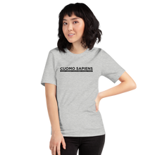 Load image into Gallery viewer, Woman wearing a heather grey unisex t-shirt, featuring the Cuomo Sapiens S.U.D.L.T. graphic in black.
