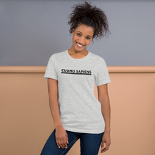 Load image into Gallery viewer, Woman standing against a wall, wearing a heather grey unisex t-shirt, featuring the Cuomo Sapiens S.U.D.L.T. graphic in black.