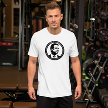 Load image into Gallery viewer, Man at the gym, wearing a white unisex t-shirt, featuring the Cuomo Sapiens S.U.D.L.T. SEAL graphic in black.