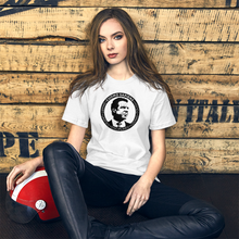 Load image into Gallery viewer, Woman with a motorcycle helmet next to some crates, wearing a white unisex t-shirt, featuring the Cuomo Sapiens S.U.D.L.T. SEAL graphic in black.