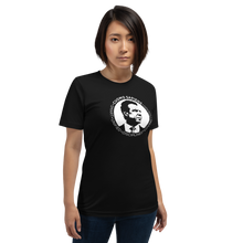 Load image into Gallery viewer, Woman wearing a black unisex t-shirt, featuring the Cuomo Sapiens S.U.D.L.T. SEAL graphic in white.
