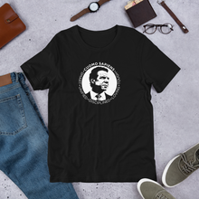 Load image into Gallery viewer, A black unisex t-shirt on the floor, featuring the Cuomo Sapiens S.U.D.L.T. SEAL graphic in white.
