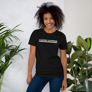 Woman standing next to some plants, wearing a black unisex t-shirt, featuring the Cuomo Sapiens S.U.D.L.T. graphic in white.