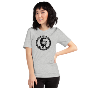 Woman wearing a heather grey unisex t-shirt, featuring the Cuomo Sapiens S.U.D.L.T. SEAL graphic in black.