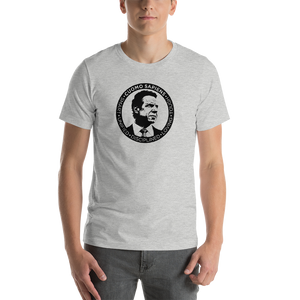 Man wearing a heather grey unisex t-shirt, featuring the Cuomo Sapiens S.U.D.L.T. SEAL graphic in black.