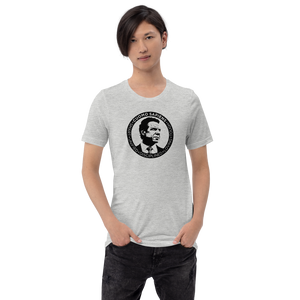 Man wearing a heather grey unisex t-shirt, featuring the Cuomo Sapiens S.U.D.L.T. SEAL graphic in black.