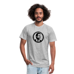 Man wearing a heather grey unisex t-shirt, featuring the Cuomo Sapiens S.U.D.L.T. SEAL graphic in black.