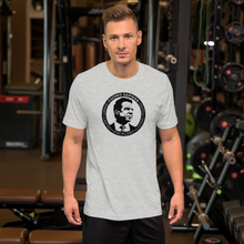 Load image into Gallery viewer, Man at the gym, wearing a heather grey unisex t-shirt, featuring the Cuomo Sapiens S.U.D.L.T. SEAL graphic in black.
