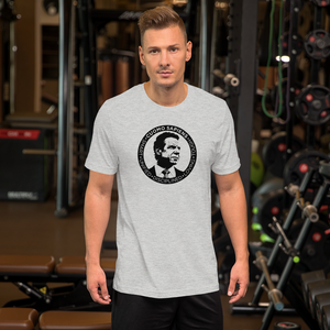 Man at the gym, wearing a heather grey unisex t-shirt, featuring the Cuomo Sapiens S.U.D.L.T. SEAL graphic in black.