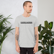Load image into Gallery viewer, Man standing next to some plants, wearing a heather grey unisex t-shirt, featuring the Cuomo Sapiens S.U.D.L.T. graphic in black.
