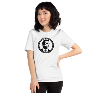 Woman wearing a white unisex t-shirt, featuring the Cuomo Sapiens S.U.D.L.T. SEAL graphic in black.