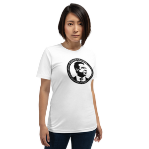 Woman wearing a white unisex t-shirt, featuring the Cuomo Sapiens S.U.D.L.T. SEAL graphic in black.