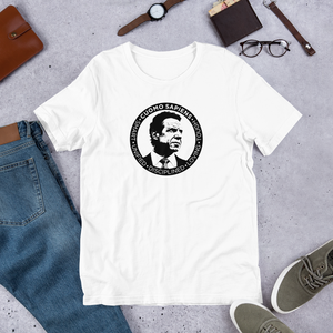 A white unisex t-shirt on the floor, featuring the Cuomo Sapiens S.U.D.L.T. SEAL graphic in black.