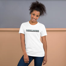 Load image into Gallery viewer, Woman standing against a wall, wearing a white unisex t-shirt, featuring the Cuomo Sapiens S.U.D.L.T. graphic in black.
