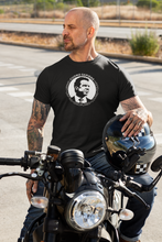 Load image into Gallery viewer, Man sitting on a motorcycle with his helmet on his knee , wearing a black unisex t-shirt, featuring the Cuomo Sapiens S.U.D.L.T. SEAL graphic in white.
